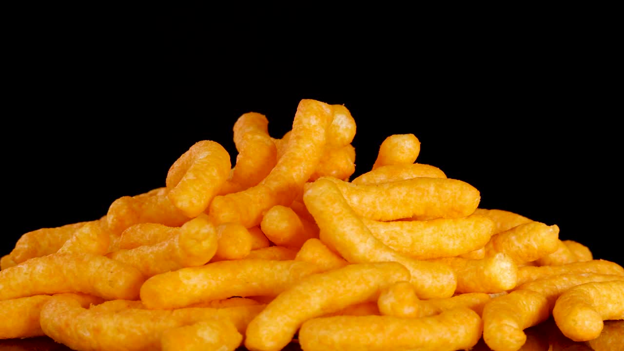 Golden cheese puffs rotate smoothly under studio lighting, highlighting crispy texture and vibrant color