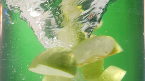 disparo estático en cámara lenta de piezas de manzana verde fresca que caen en un remolino de agua y comienzan a girar en un círculo contra un fondo verde