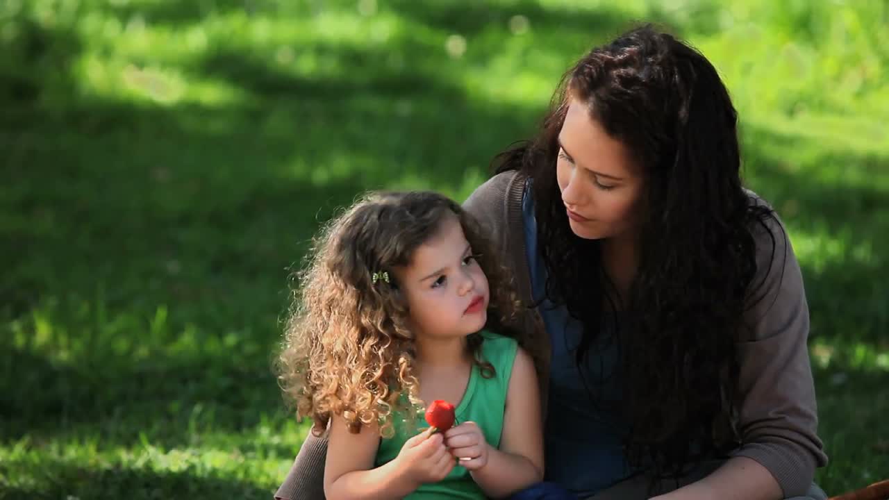 mamá y hija disfrutando de fresas sentadas en el césped