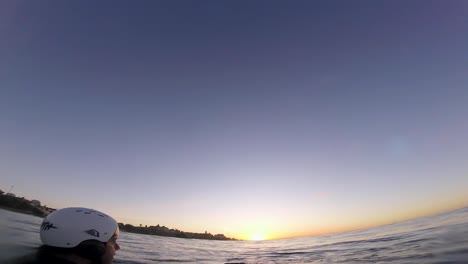 Young-causasian-man-surfer-sits-on-the-line-up-during-morning-surf-session,-waits-his-wave-and-enjoys-warm-tropical-sunrise