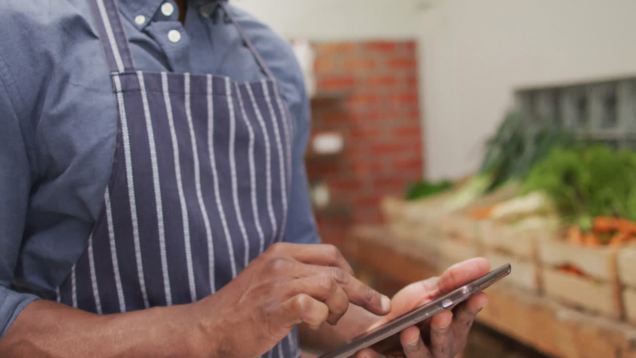 Video of happy african american salesman using tablet in organic grocery shop