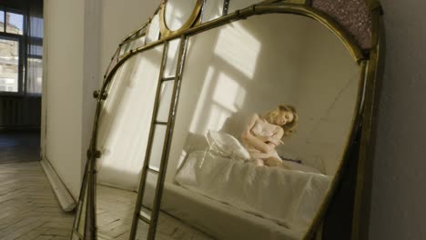 woman sitting in a bed, reflected in an ornate mirror, bathed in sunlight