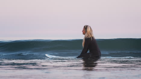 Frau-Im-Neoprenanzug-Sitzt-Und-Schwimmt-Auf-Einem-Surfbrett-Im-Meer,-Während-Um-Sie-Herum-Wellen-Brechen