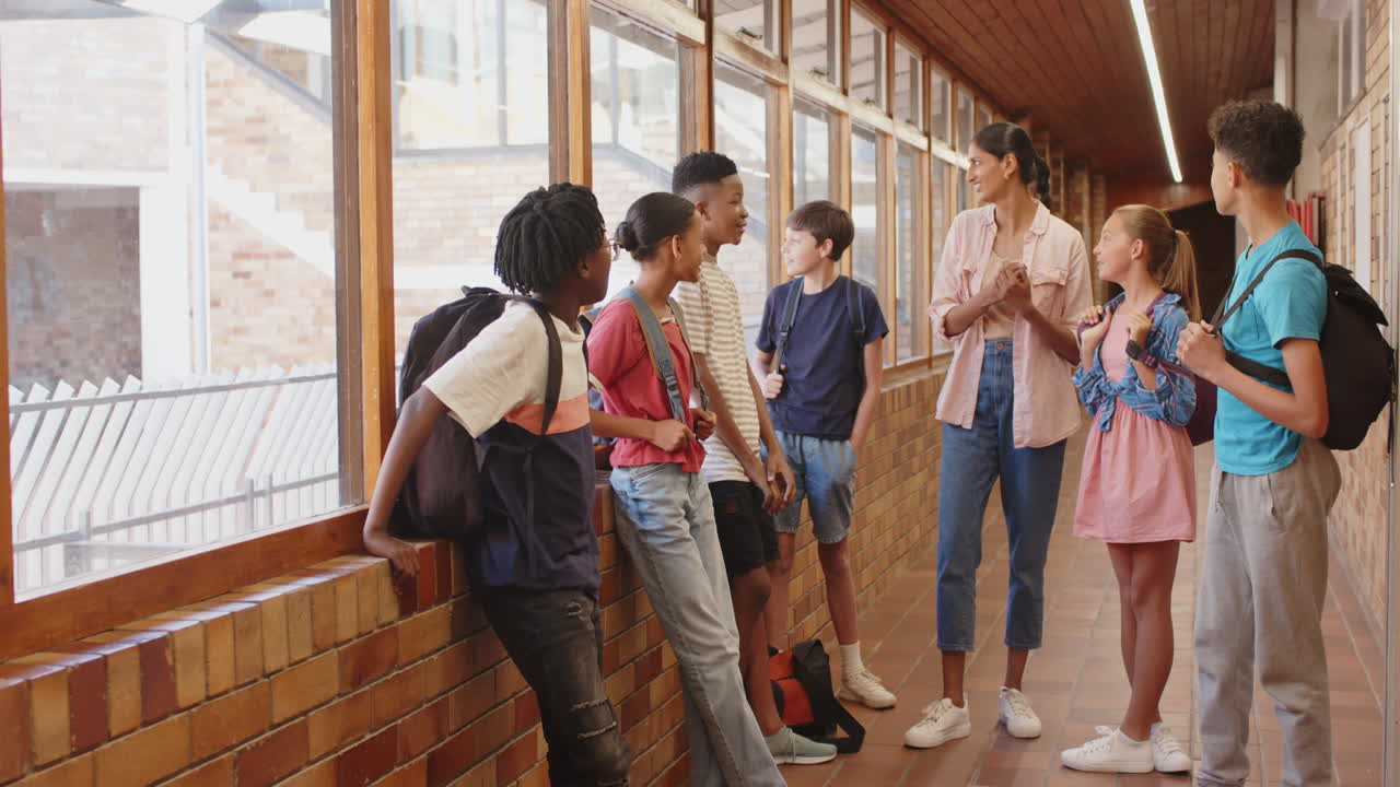 In school hallway, group of students talking and laughing with teacher