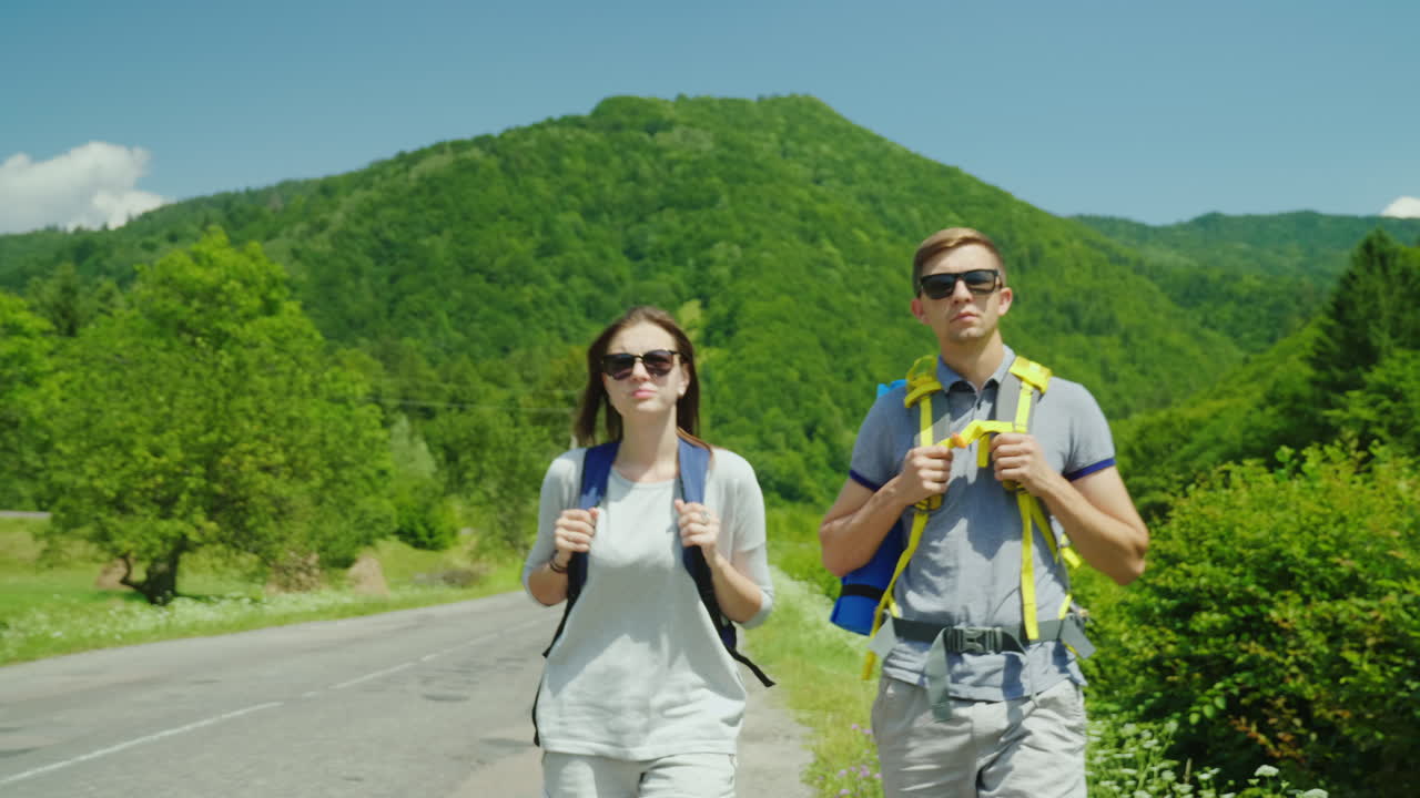 una joven pareja de turistas camina por el camino hacia hermosas montañas cubiertas de bosques forma activa de