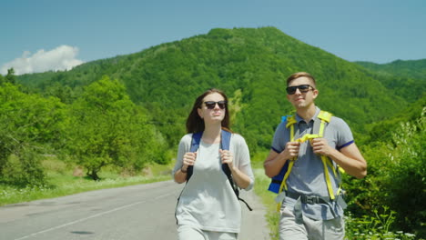 Ein-Junges-Touristenpaar-Geht-Die-Straße-Entlang-Zu-Wunderschönen-Bergen,-Die-Mit-Wald-Bedeckt-Sind