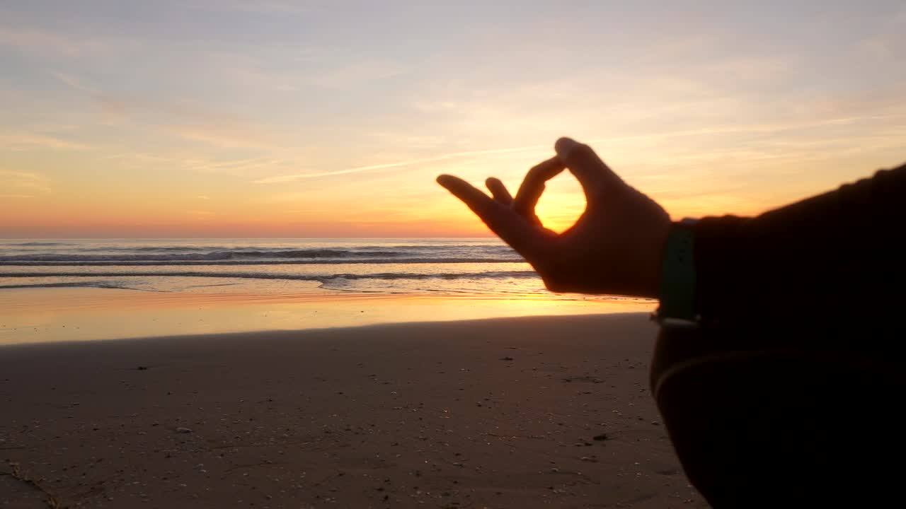 silueta de la mano de una mujer que está haciendo yoga frente al mar