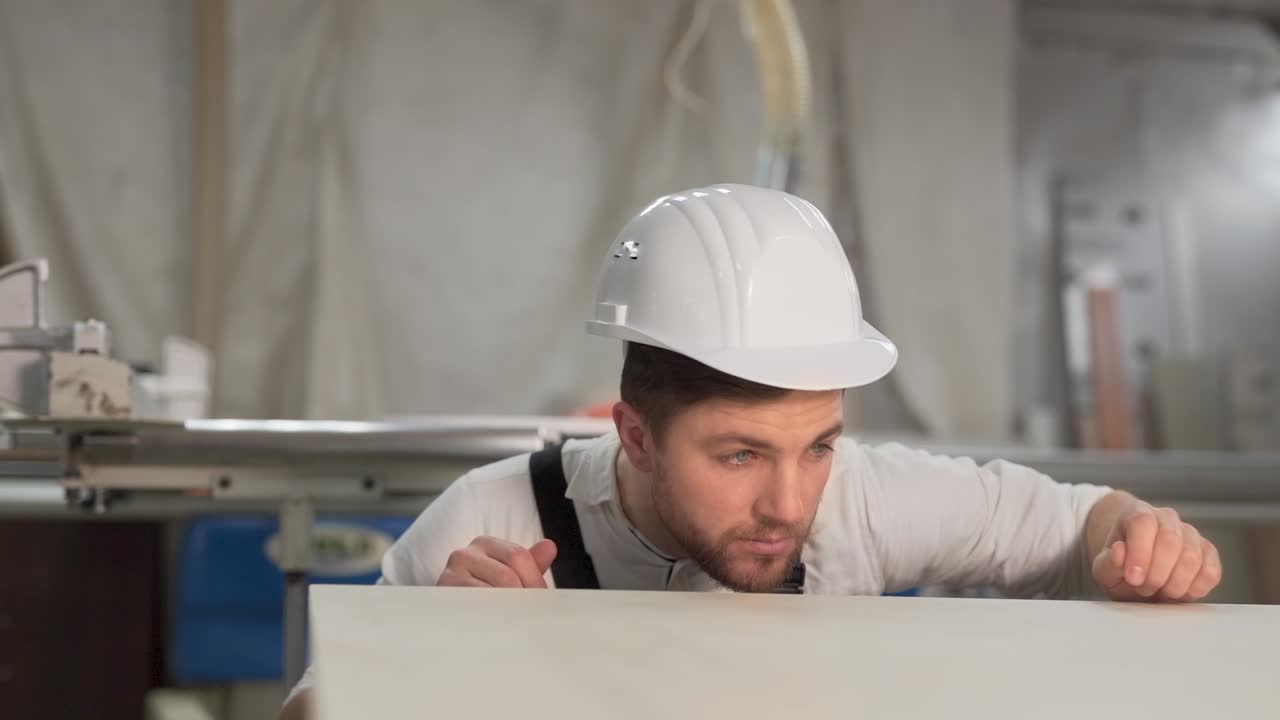 el carpintero en el casco en la fábrica comprueba la uniformidad de la superficie del material