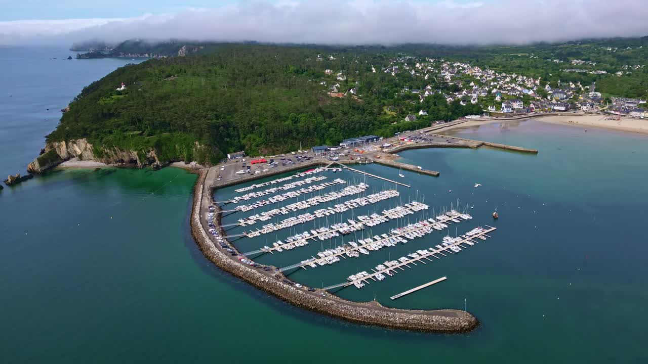 Drone pulling back over Morgat marina in Crozon, showing the harbor, breakwater, coastline, vegetation and distant houses - Brittany France