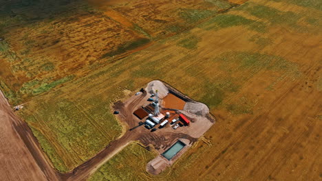distancing form the gas extracting company located in the vast field. single derrick with drilling equipment and pool with water in are at the site. aerial view.