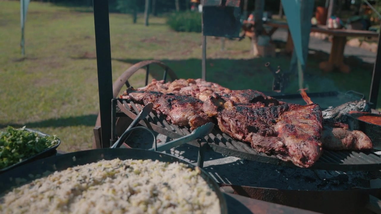 Primer plano de auténtico asado argentino a la parrilla con carne al aire libre en un entorno rústico de pícnic.