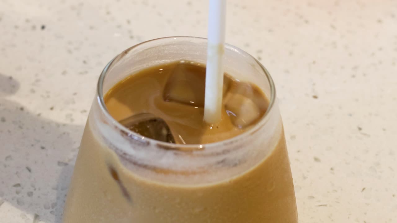 Hand stirring iced coffee with a straw