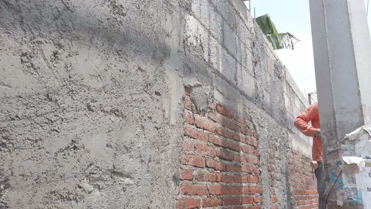 Worker applying cement to brick and cinder block wall under sunny outdoor light