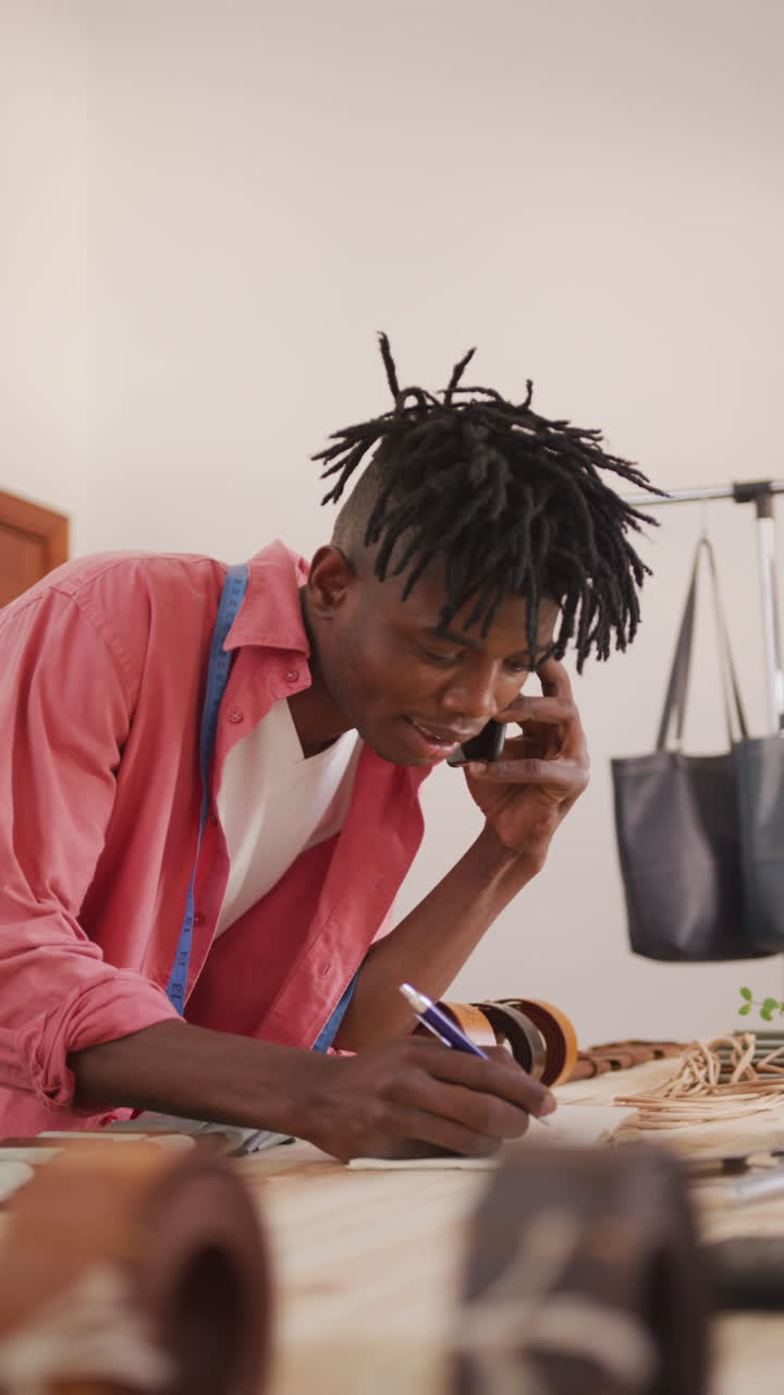 Video verticale di un artigiano del cuoio afroamericano felice con i dreadlock al telefono in laboratorio