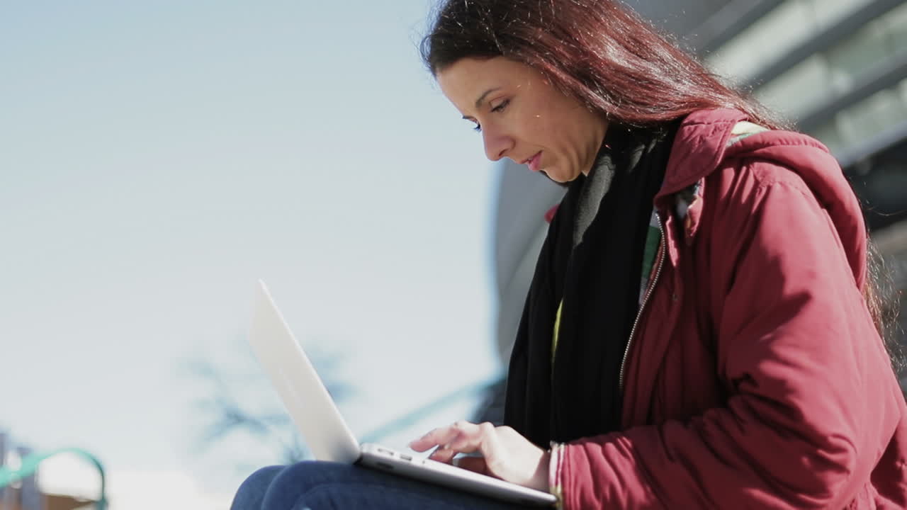 Side view of confident middle aged woman typing on laptop outdoor