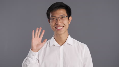 Asian-man-smiling-and-waving-to-the-camera.