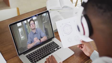 African-american-businessman-sitting-at-desk-using-laptop-having-video-call-with-male-colleague