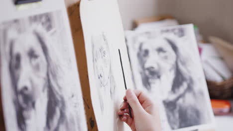 close up of artist sitting at easel drawing picture of dog in charcoal from photograph