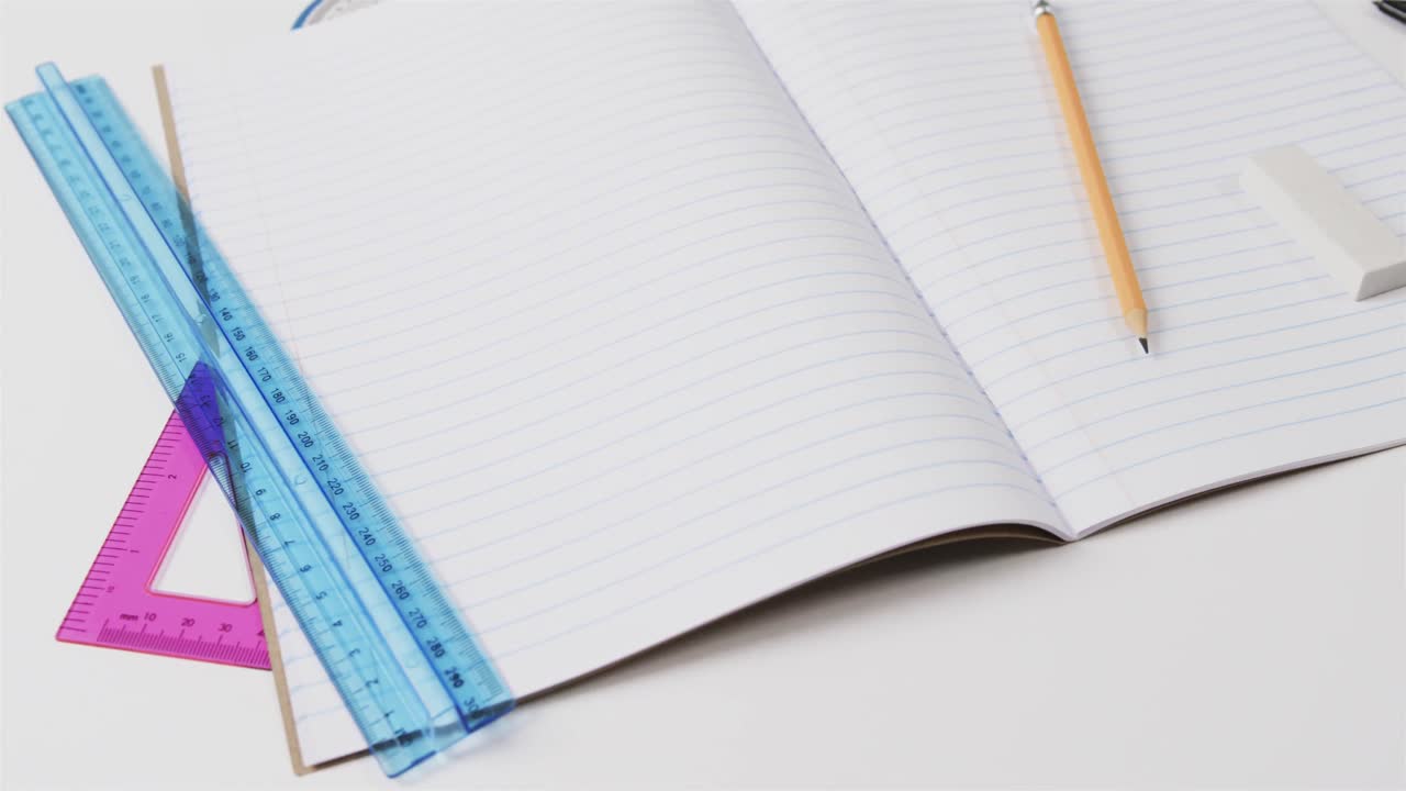 Close up of open notebook with school stationery on grey background, in slow motion