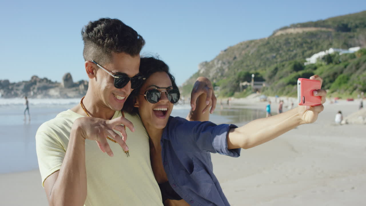 hermosa pareja de raza mixta tomando selfies en la playa tirando caras divertidas