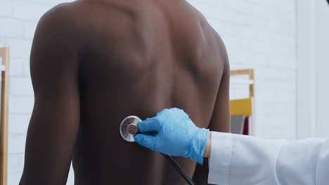 doctor examining patient's back with stethoscope