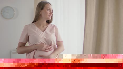 woman in her baby's room touching her tummy and looking out the window