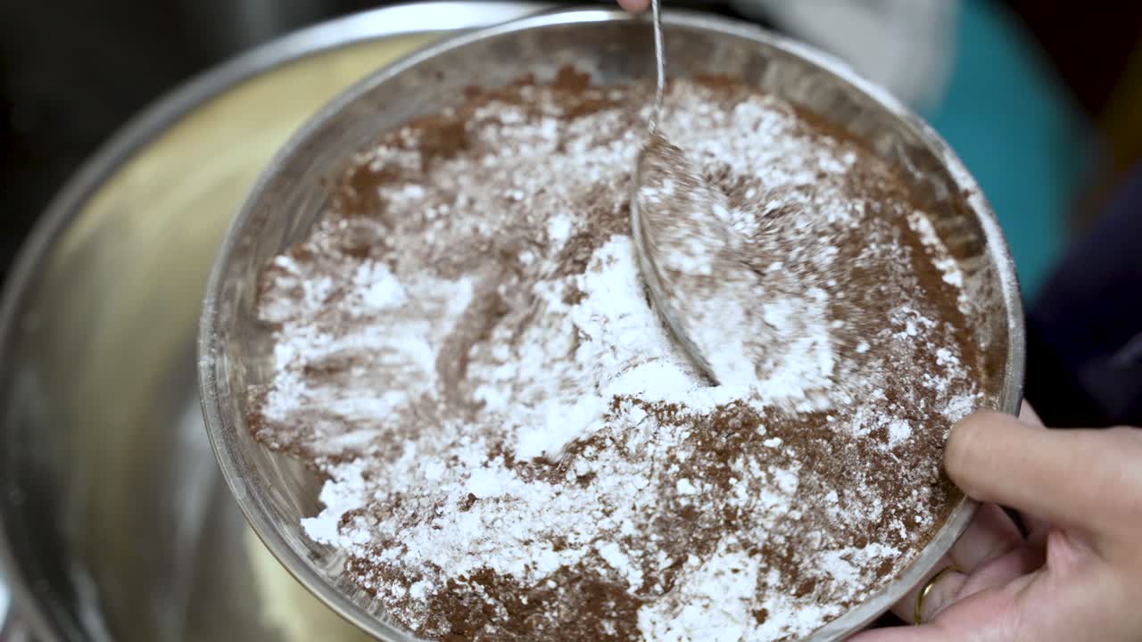 Close up of a pastry chef mixing flour and cocoa powder with a spoon, preparing ingredients for baking a cake. slow motion