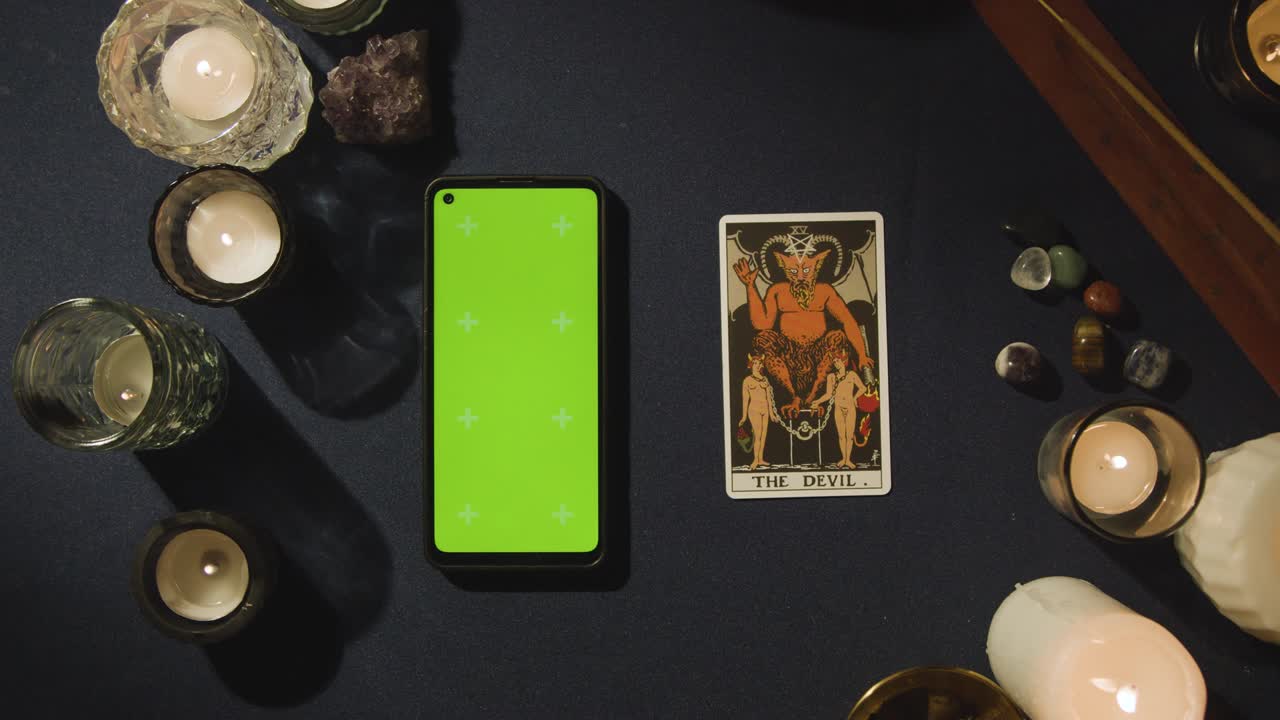 disparo aéreo de una persona que da lectura de tarot con pantalla verde teléfono móvil al lado de la tarjeta del diablo en la mesa