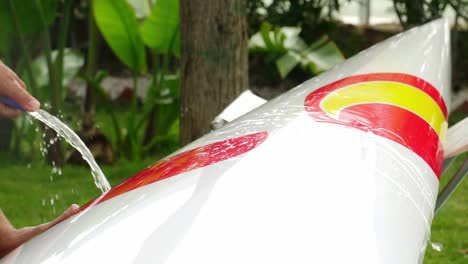 close-up of a person hosing down a nice and new professional canoe in slow motion in a garden