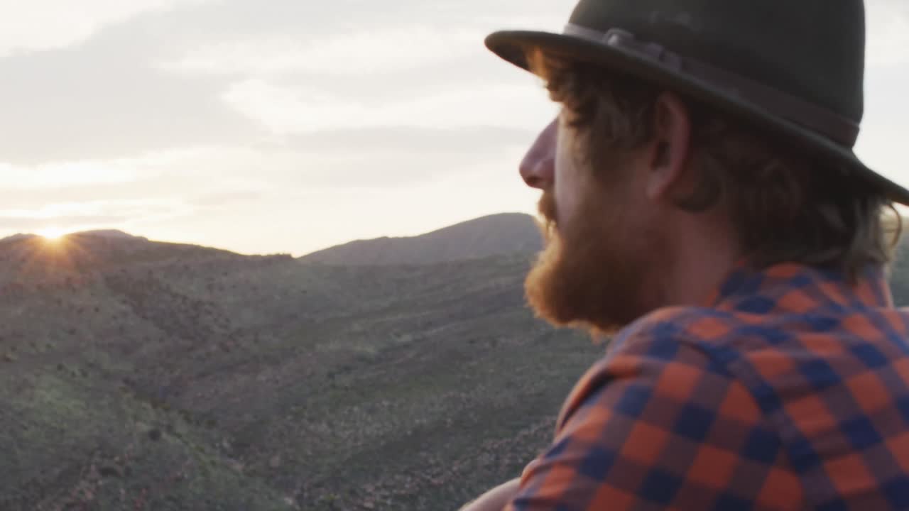 hombre caucásico barbudo sobreviviente admirando la vista desde el pico de la montaña en el desierto