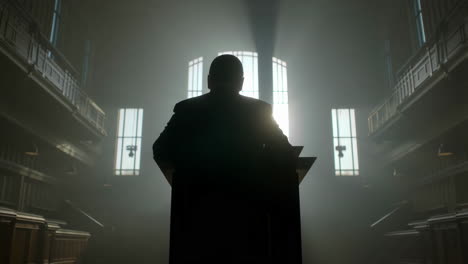 backlit silhouette of a speaker at a podium in a grand hall