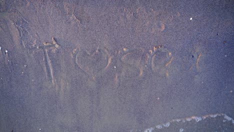 handwritten drawings on sandy beach. water waves breaking the symbol on sand and wash it away. top view.