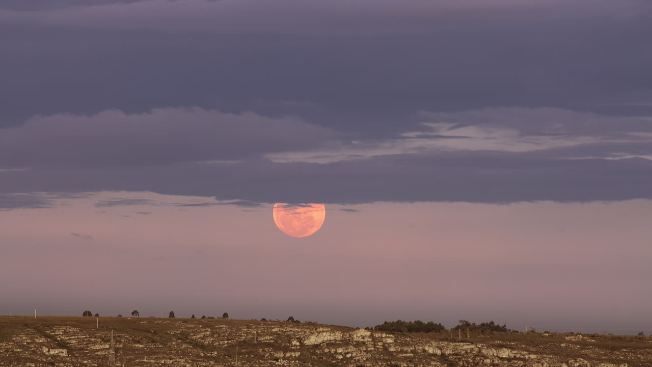 восход полной светящейся красной луны с облаками над горизонтом земли