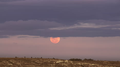 Ascenso-De-Una-Luna-Roja-Brillante-Con-Nubes-Sobre-El-Horizonte-De-La-Tierra