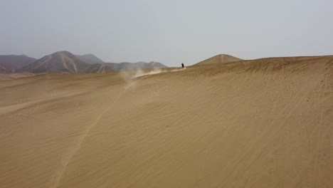 Toma-De-Drones-De-Una-Sola-Motocicleta-A-Lo-Lejos-Viajando-Por-Dunas-De-Arena-Del-Desierto.