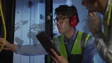 spinning globe and world map against diverse male and female engineers working in server room