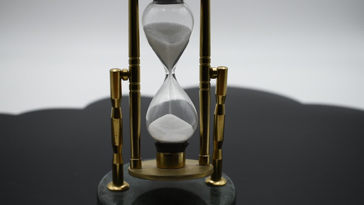 Sand running through the bulbs of an hourglass measuring the passing time on a black and white background