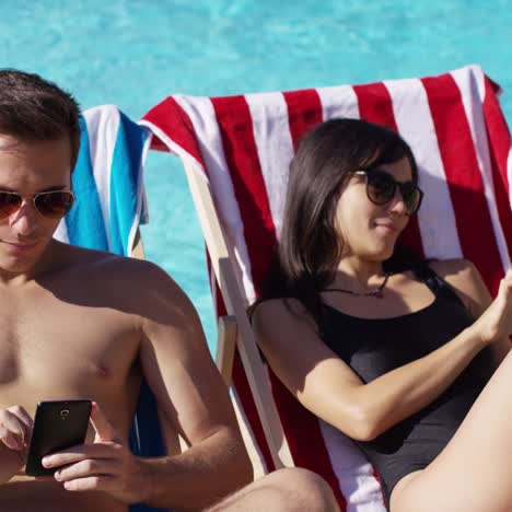 Young-couple-using-phones-at-the-swimming-pool