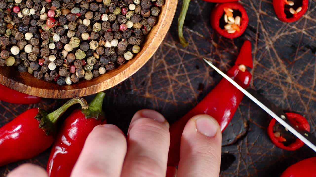 Men's hands cut off from red chili peppers little pieces.