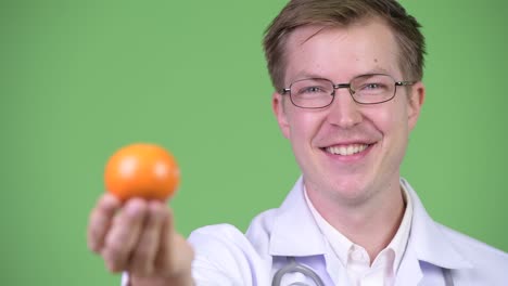 portrait of young man doctor holding orange fruit