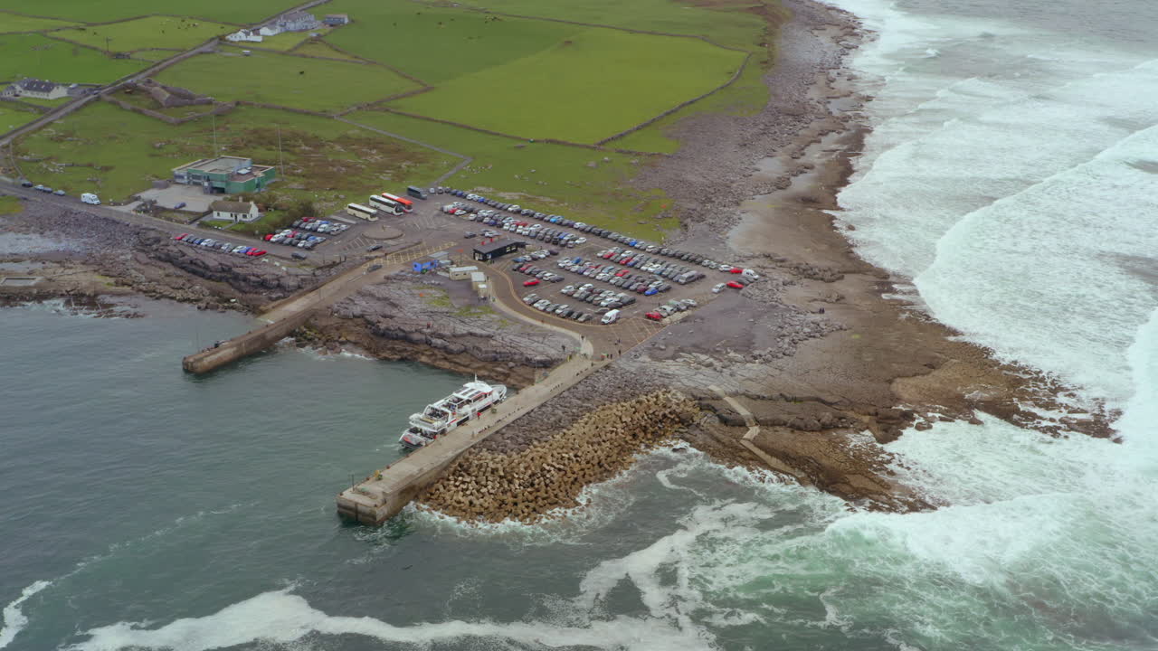 Aerial view of Aran ferry docking at Doolin pier with Atlantic waves and parking lot in vast view