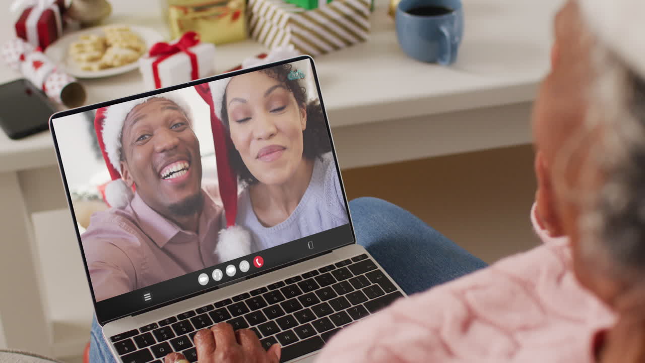 mujer afroamericana senior con sombrero de santa teniendo llamada de video portátil con pareja feliz diversa