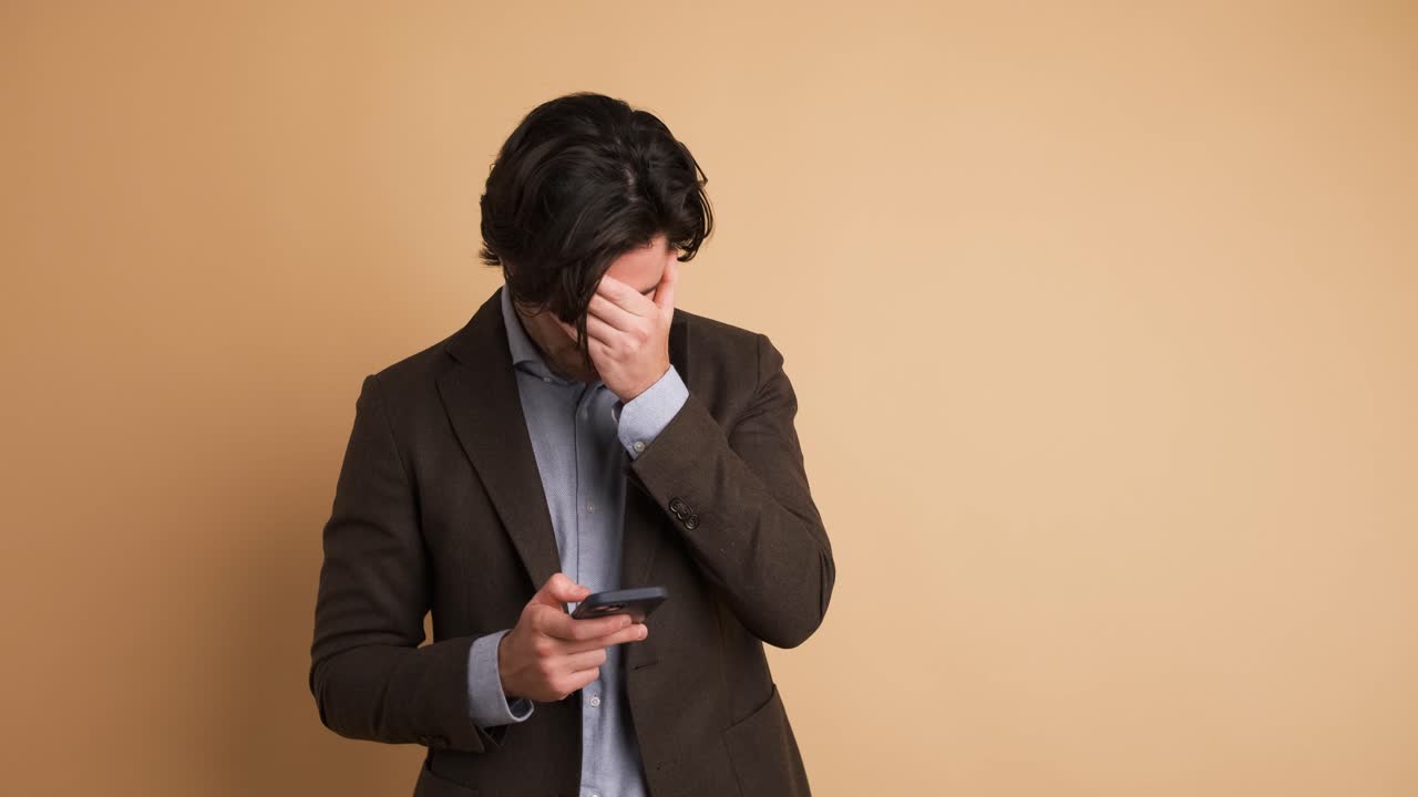 Businessman feeling upset about losing lottery on smartphone in brown studio
