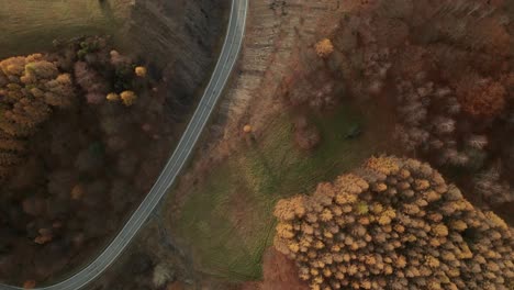 an aerial tilt down drone view of a winding road running through a canyon in late autumn