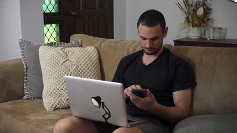 man using laptop and phone sitting on couch