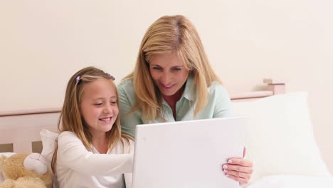 mother and daughter using laptop together on bed