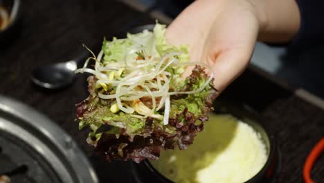 person making lettuce leaf ssam - korean pork belly barbecue wrapped in lettuce with ssamjang