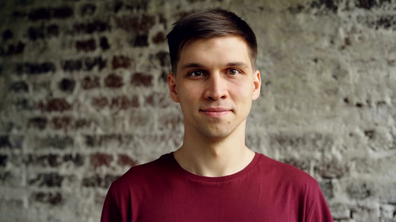 retrato en primer plano de un joven guapo de cabello oscuro con una camiseta brillante sonriendo y mirando a la cámara. gente joven, estilo loft interior y concepto de felicidad.
