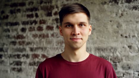 close-up portrait of dark-haired handsome young man in bright t-shirt smiling and looking at camera. young people, loft style interior and happiness concept.