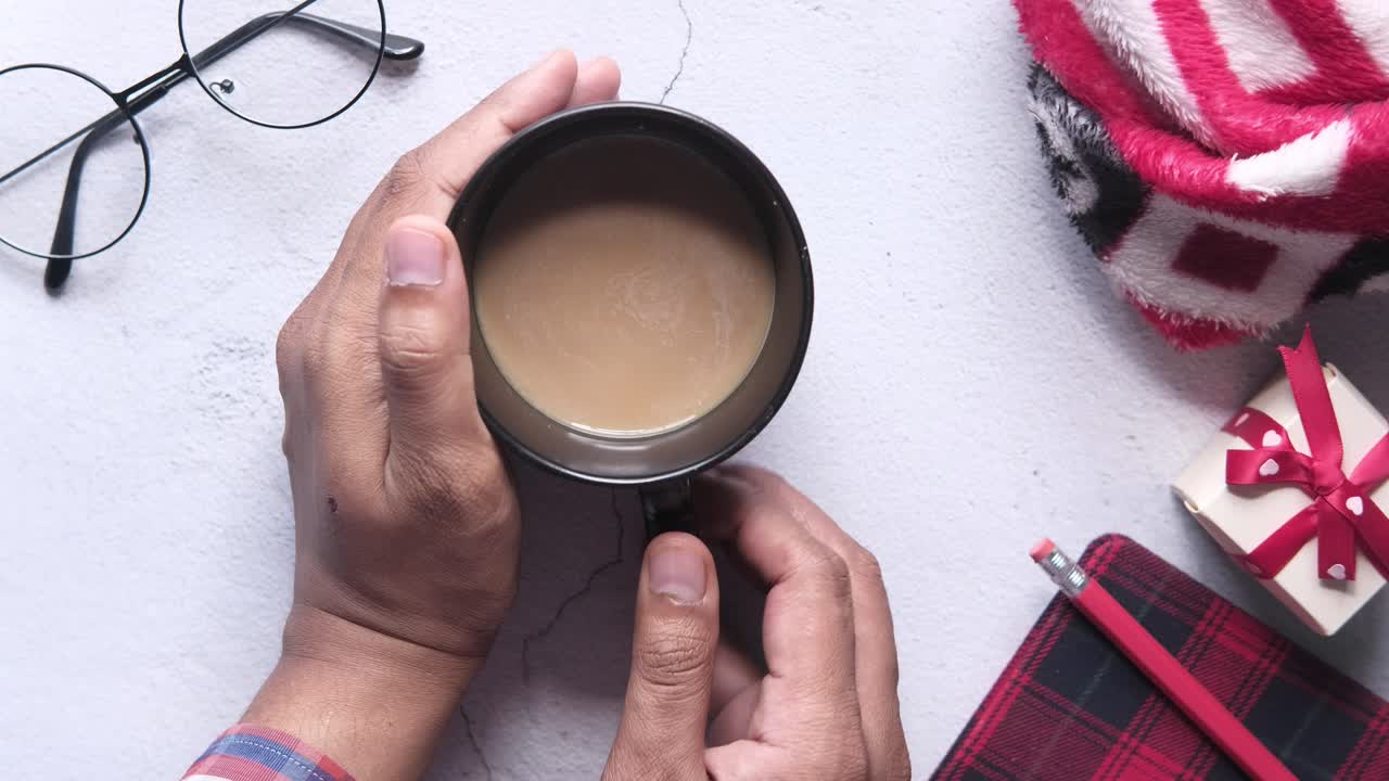 커피 컵, 안경, 선물 상자, 그리고 책상 위에 담요를 들고 있는 사람.